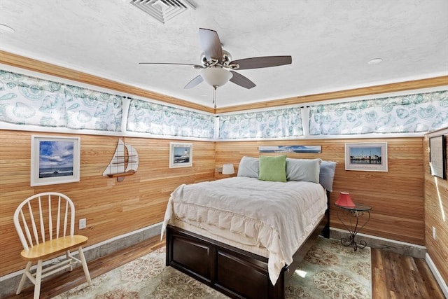 bedroom with ceiling fan, wood-type flooring, and wooden walls