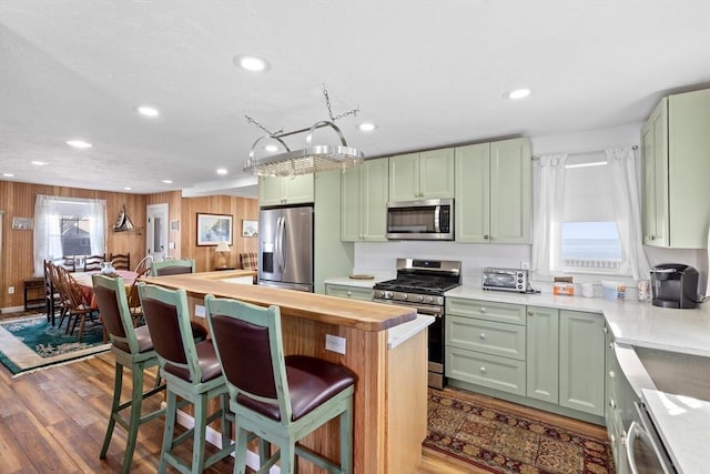 kitchen featuring a breakfast bar area, butcher block counters, green cabinets, and stainless steel appliances