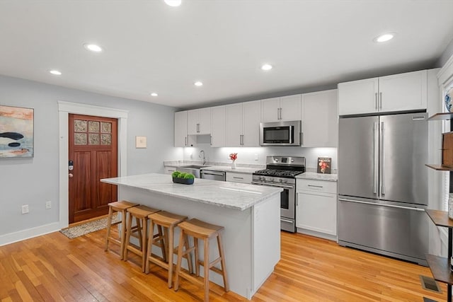 kitchen featuring a center island, white cabinetry, light hardwood / wood-style flooring, a breakfast bar, and stainless steel appliances