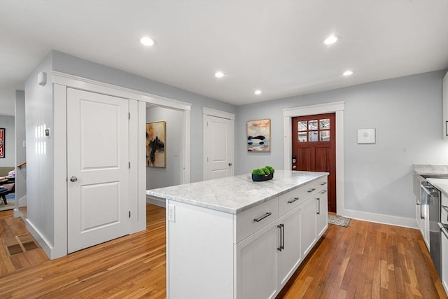 kitchen featuring light stone counters, white cabinets, a center island, and light wood-type flooring