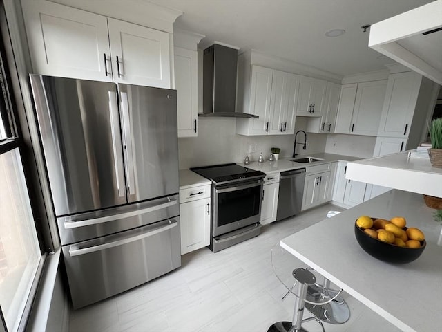 kitchen with wall chimney range hood, light countertops, stainless steel appliances, white cabinetry, and a sink