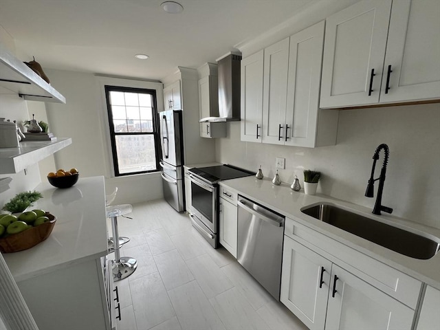 kitchen with light countertops, appliances with stainless steel finishes, white cabinets, wall chimney exhaust hood, and a sink