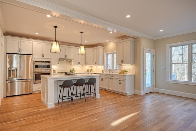 kitchen featuring appliances with stainless steel finishes, light hardwood / wood-style flooring, white cabinets, a center island, and hanging light fixtures