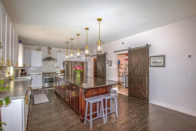 56 Otis-Tolland Rd, Blandford, MA 01008 - kitchen featuring appliances with stainless steel finishes, wall chimney exhaust hood, a barn door, dark wood-type flooring, and decorative backsplash