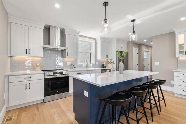 110 Fayette Unit 110, Watertown, MA 02472 - kitchen featuring wall chimney exhaust hood, a sink, a kitchen bar, stainless steel appliances, and light wood-style flooring
