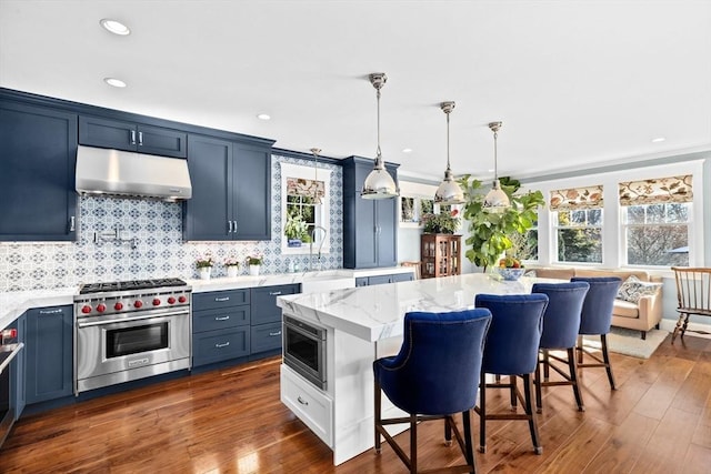 kitchen featuring a breakfast bar, under cabinet range hood, a sink, appliances with stainless steel finishes, and light stone countertops