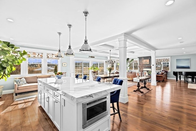 kitchen with stainless steel microwave, dark wood-type flooring, open floor plan, and decorative columns