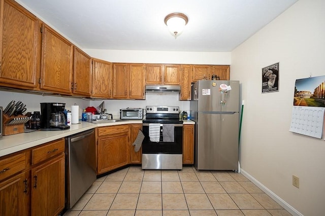 kitchen with stainless steel appliances, under cabinet range hood, brown cabinetry, light countertops, and light tile patterned floors