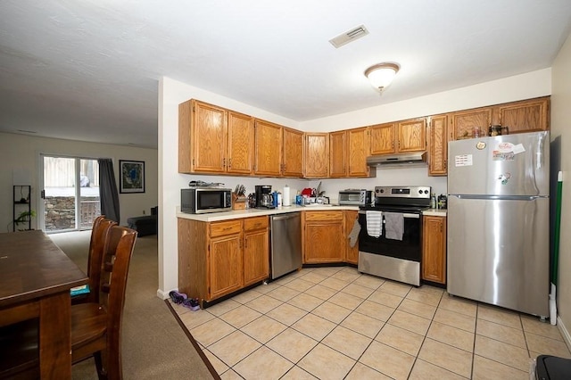 kitchen featuring appliances with stainless steel finishes, under cabinet range hood, brown cabinetry, and light countertops