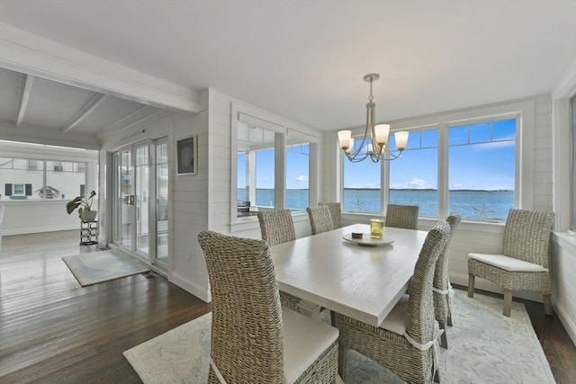 dining room featuring an inviting chandelier, beam ceiling, dark wood-type flooring, and a water view