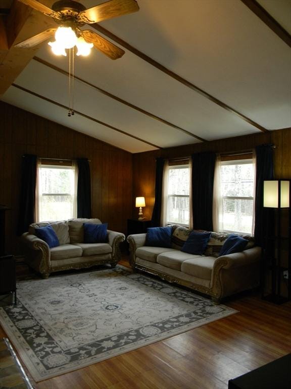 living room with a healthy amount of sunlight, lofted ceiling with beams, a ceiling fan, and wooden walls