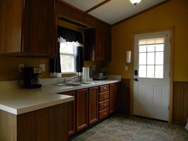 kitchen featuring light countertops, vaulted ceiling, wainscoting, and a sink