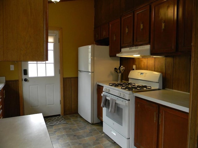 kitchen with light countertops, a wainscoted wall, under cabinet range hood, and white range with gas cooktop