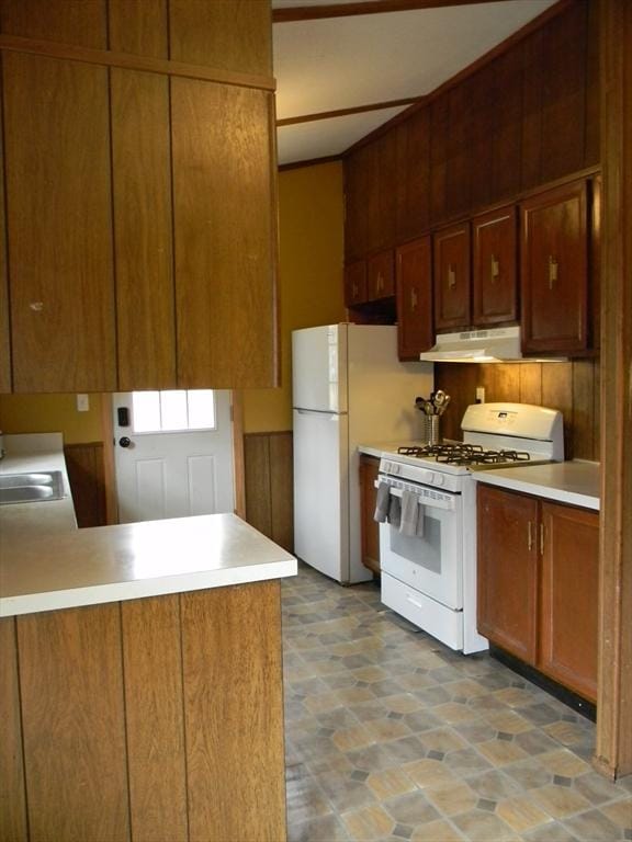 kitchen featuring brown cabinetry, light countertops, a peninsula, under cabinet range hood, and white appliances