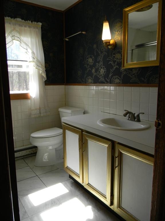 bathroom with vanity, wainscoting, toilet, tile walls, and wallpapered walls