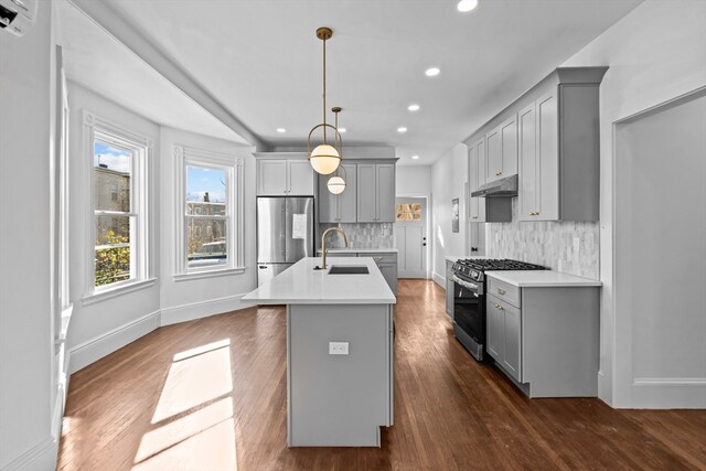 kitchen featuring sink, stainless steel appliances, dark hardwood / wood-style flooring, pendant lighting, and a kitchen island with sink