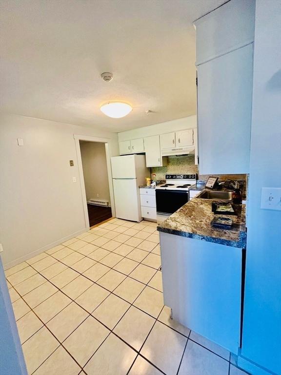 kitchen with sink, dark stone countertops, light tile patterned floors, white appliances, and white cabinets