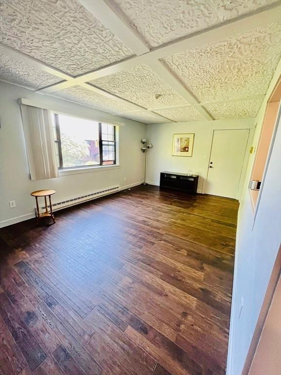 unfurnished living room featuring coffered ceiling, a baseboard heating unit, and dark wood-type flooring