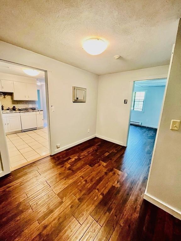 unfurnished room featuring light hardwood / wood-style flooring, a baseboard radiator, and a textured ceiling