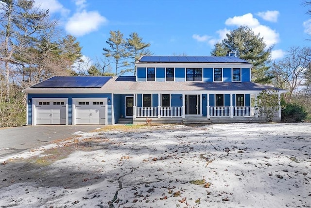 view of front of home featuring aphalt driveway, a porch, an attached garage, and roof mounted solar panels