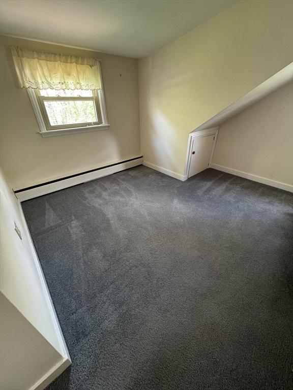 spare room with baseboards, dark colored carpet, and a baseboard heating unit