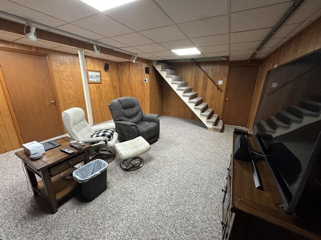 carpeted living area featuring stairs, wooden walls, and a paneled ceiling