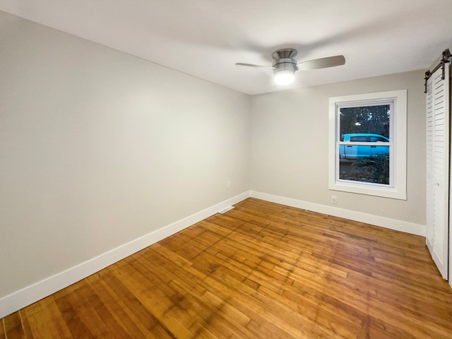 unfurnished room with hardwood / wood-style floors, ceiling fan, and a barn door