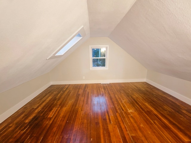 additional living space featuring vaulted ceiling with skylight, dark hardwood / wood-style floors, and a textured ceiling