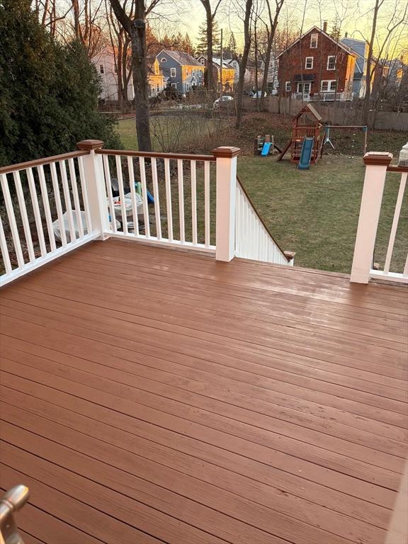 deck at dusk featuring a playground and a yard