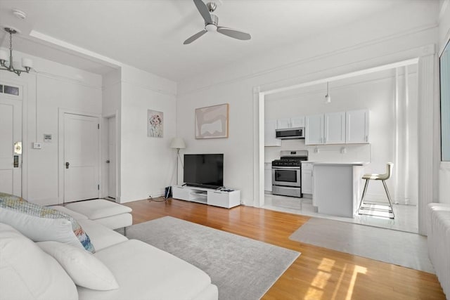 living room with ceiling fan with notable chandelier and light wood-type flooring