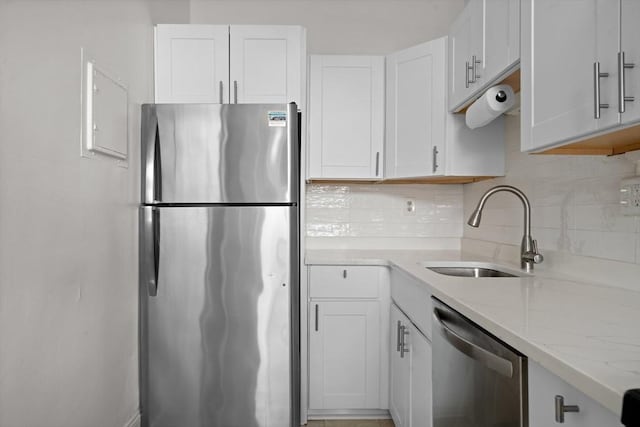 kitchen with light stone countertops, backsplash, white cabinetry, appliances with stainless steel finishes, and sink