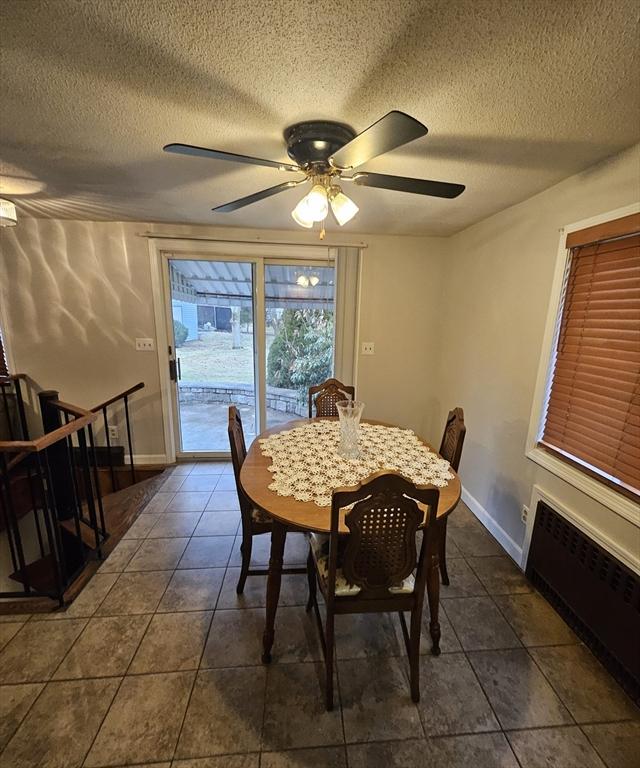 dining space with dark tile patterned floors, radiator heating unit, baseboards, and a textured ceiling