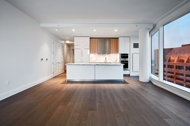 kitchen featuring tasteful backsplash, white cabinets, a center island with sink, and dark hardwood / wood-style flooring