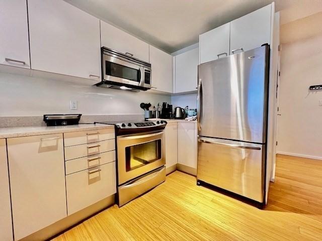 2 Earhart Unit 121, Cambridge, MA 02141 - kitchen featuring appliances with stainless steel finishes, light wood-style floors, light countertops, and baseboards