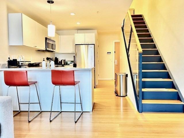 2 Earhart Unit 121, Cambridge, MA 02141 - kitchen with appliances with stainless steel finishes, a peninsula, a breakfast bar, white cabinets, and light wood-type flooring