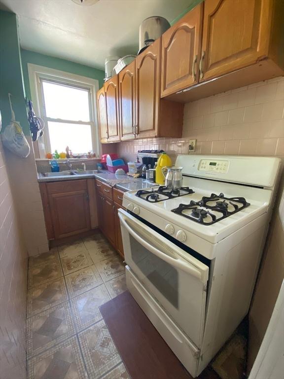 kitchen with white range with gas cooktop, brown cabinetry, and tasteful backsplash