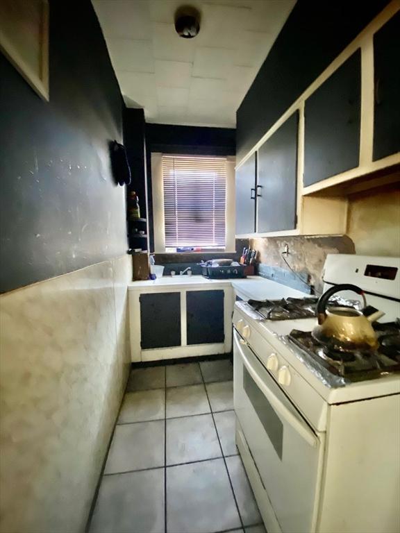 kitchen with white range with gas cooktop, light tile patterned flooring, and decorative backsplash