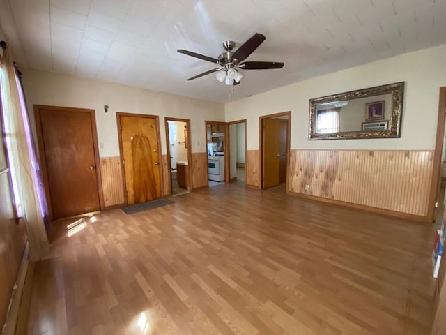 interior space with ceiling fan, a wainscoted wall, wood walls, and light wood finished floors