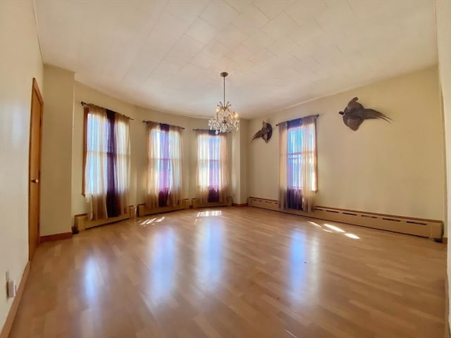 spare room featuring an inviting chandelier, baseboard heating, wood finished floors, and baseboards