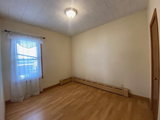 unfurnished room with a baseboard heating unit, baseboards, and light wood-type flooring