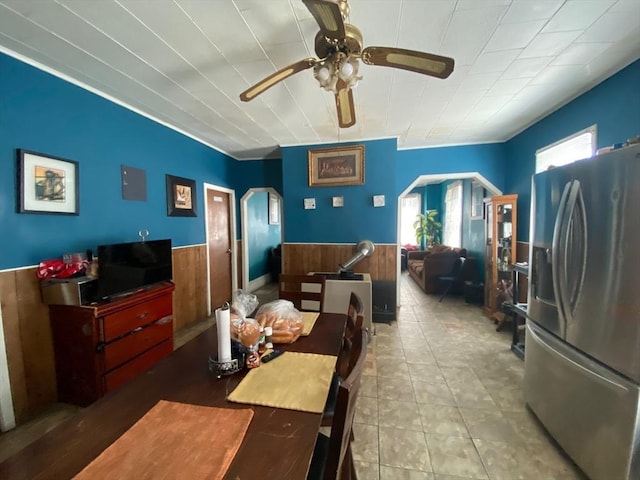 dining room with a ceiling fan, arched walkways, and wainscoting