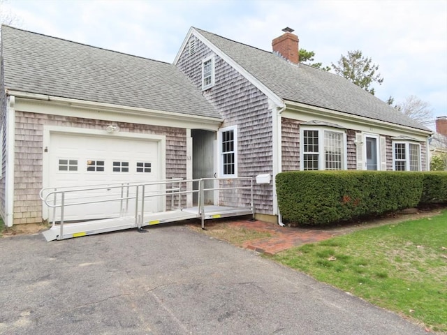 new england style home featuring a chimney, a garage, driveway, and roof with shingles