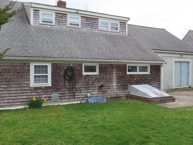 rear view of property featuring a chimney, a yard, and a shingled roof