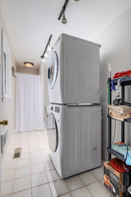 clothes washing area featuring light tile patterned flooring and stacked washing maching and dryer