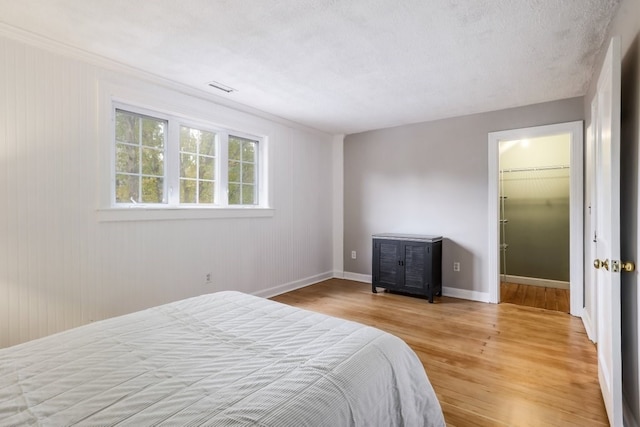 bedroom with a textured ceiling, light wood-type flooring, a closet, and a walk in closet