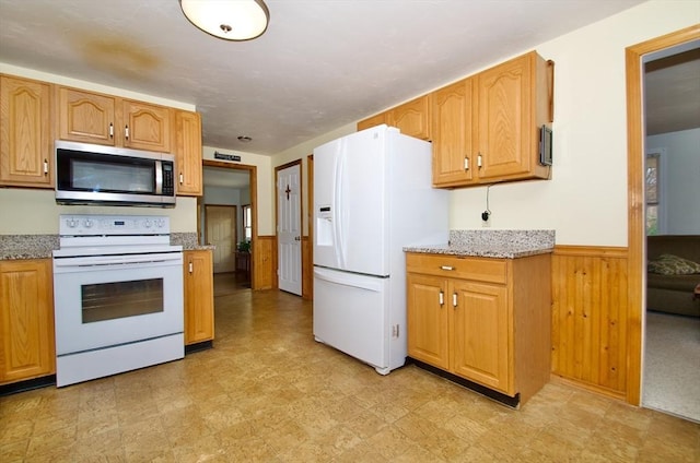 kitchen with light stone counters, white appliances, and wooden walls