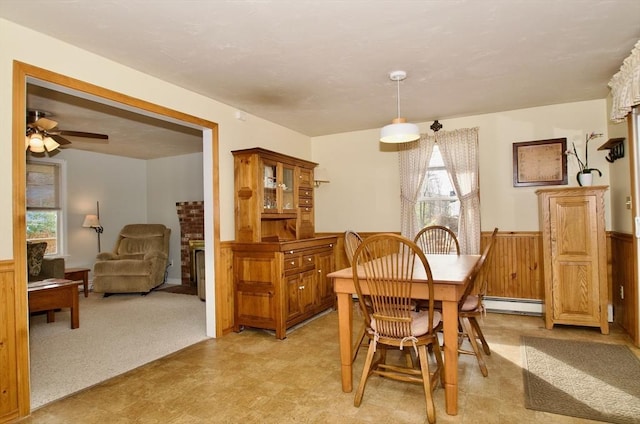 carpeted dining space with ceiling fan, baseboard heating, and wood walls