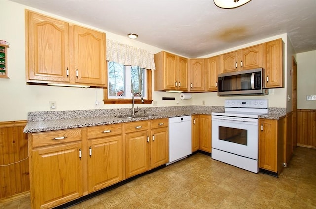 kitchen featuring sink, wooden walls, light stone counters, and white appliances