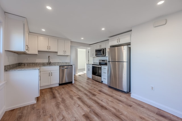 kitchen featuring sink, light stone counters, light hardwood / wood-style flooring, white cabinets, and appliances with stainless steel finishes