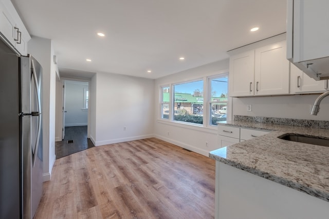 kitchen with light stone countertops, sink, light hardwood / wood-style flooring, stainless steel fridge, and white cabinets